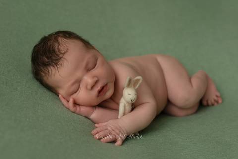 baby lying to side holding a bunny'