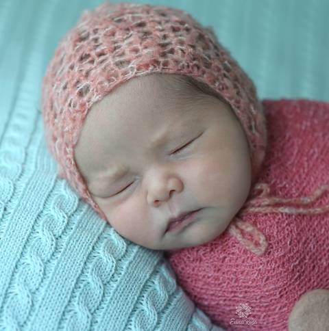 foto do rosto do bebe enrolado em wrap rosa com toquinha'