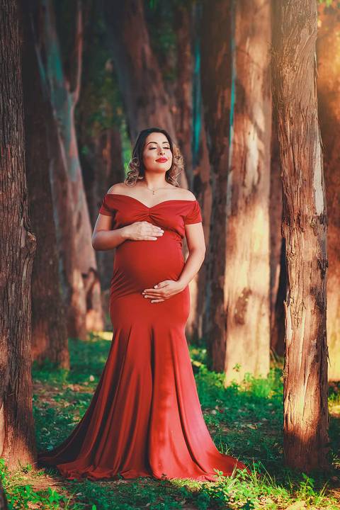 gestante de vestido vermelho e olho fechados, com as mãos na barriga, no Parque dos Ipes, em Santa Bárbara d'Oeste - SP'