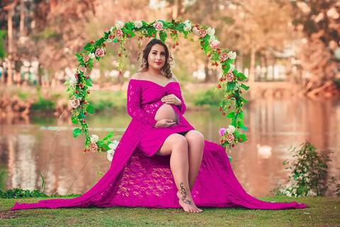 gestante no arco de flores com as mãos na barriga e vestido rosa, no Parque dos Ipes, em Santa Bárbara d'Oeste - SP'