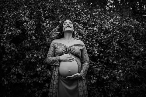 mamãe com s mãos na barriga e sorrindo, jogando os cabelos para os lados, em preto e branco, no Parque dos Ipes, em Santa Bárbara d'Oeste - SP'