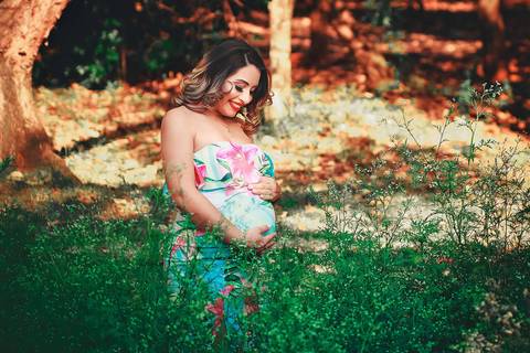 gestante sorrindo olhando para sua barriga com bastante matinhos em volta, no Parque dos Ipes, em Santa Bárbara d'Oeste - SP'