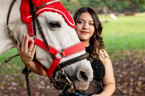 Isa, em seu ensaio de 15 anos em Ribeirão Preto, demonstra toda sua paixão e carinho pelo cavalo que marcou este momento especial. O close revela a conexão única entre os dois, com destaque para o vestido preto elegante e a delicadeza do toque, mostrando '