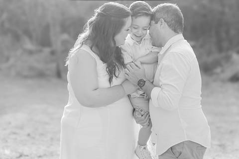 Fotógrafo de casamento em Ribeirão Preto captura Thays e Lucas abraçando o filho com risos, um retrato de família em preto e branco.'