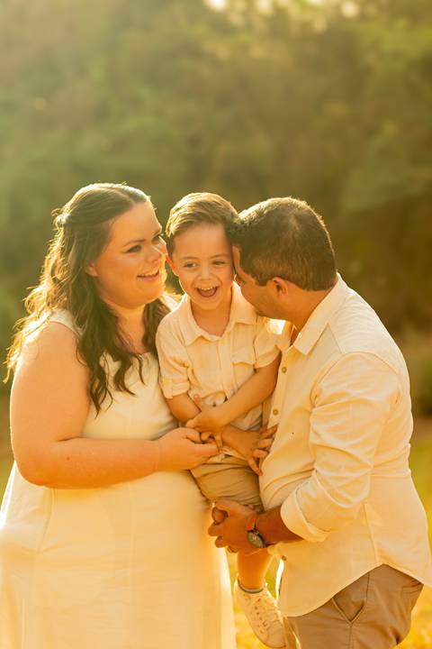 Fotógrafo de casamento em Ribeirão Preto captura Thays e Lucas abraçando o filho com risos, um retrato de família em preto e branco.'