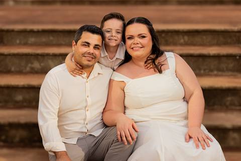 Fotógrafo de casamento em Ribeirão Preto captura Thays e Lucas abraçando o filho com risos, um retrato de família em preto e branco.'