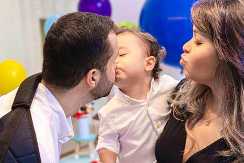 filho criança no colo da mãe beijando o pai '