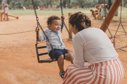 mãe brincando com filho no balanço do parquinho'