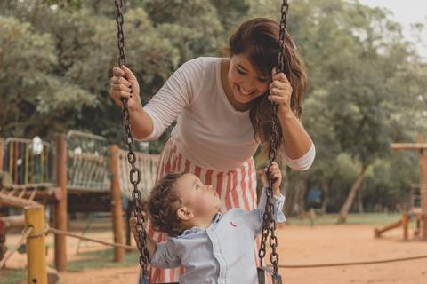 mãe brincando com filho no balanço do parquinho'