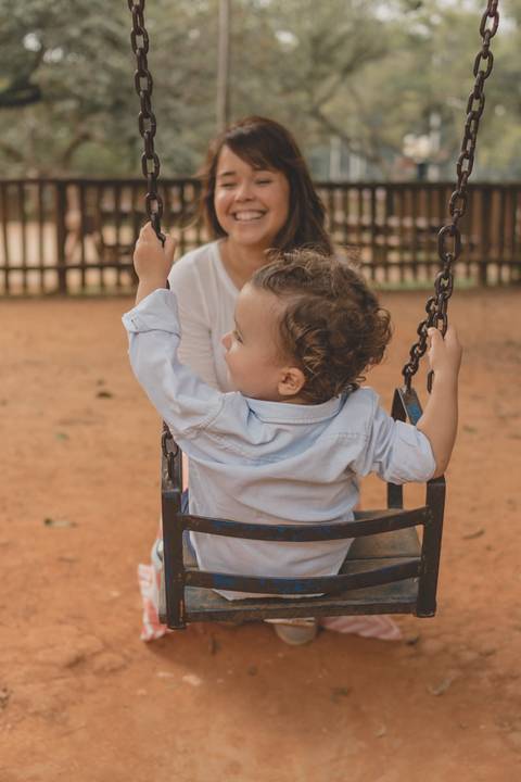 mãe brincando com filho no balanço do parquinho'