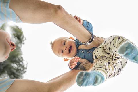Pai levantando filho bebê no colo no alto'