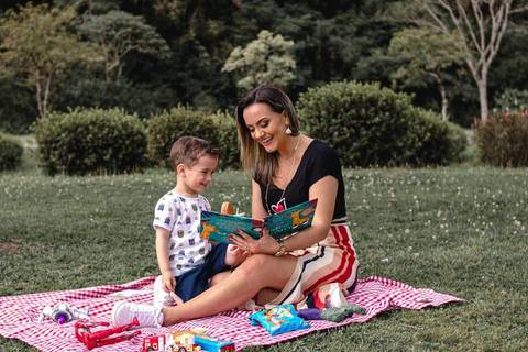 mãe e filho lendo livro no gramado do parque '