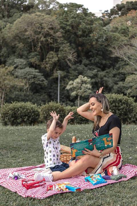mãe e filho lendo livro no gramado do parque '