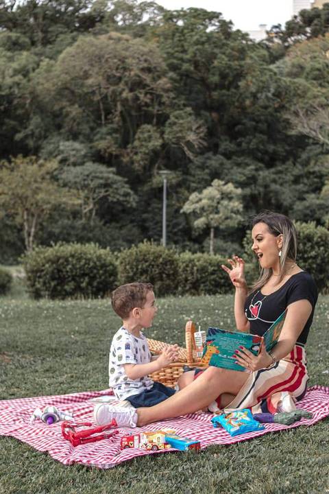 mãe e filho lendo livro no gramado do parque '