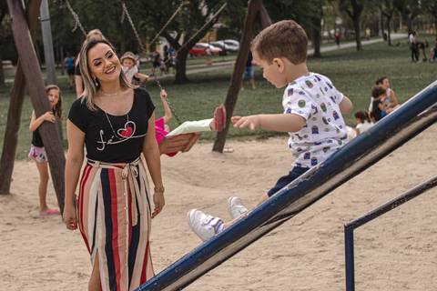 mãe olhando filho descendo no escorregador no parquinho'