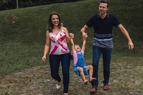 pai e mãe balançando filha pelos braços'