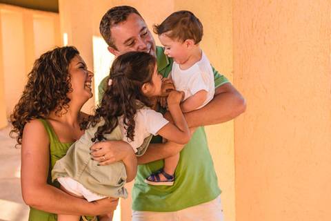 filha brincando com irmão no colo dos pais '