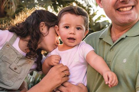 irmã brincando com irmão mais novo no colo dos pais'