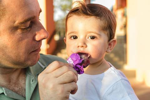 bebê chupando sorvete picolé no colo do pai '