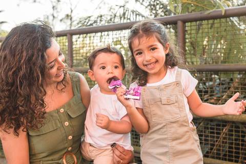 irmã dando picolé para irmão menor no colo da mãe '