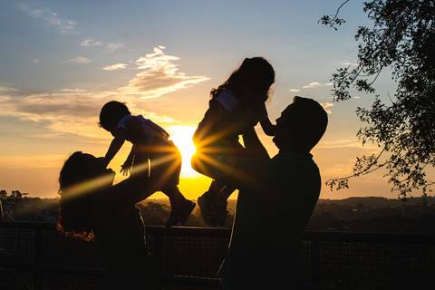 silhueta de pai e mãe levantando filhos nos braços no pôr do sol no parque '