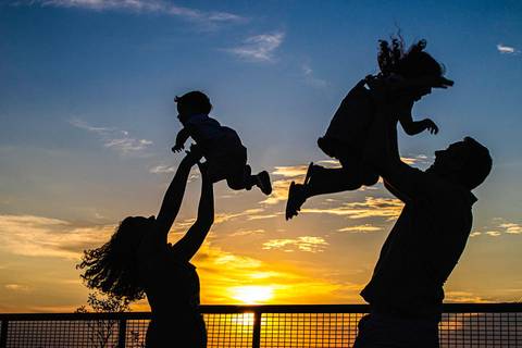 silhueta de pai e mãe levantando filhos nos braços no pôr do sol no parque '
