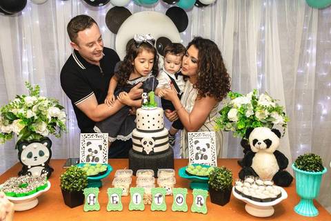 família cantando parabéns  na mesa de aniversário de um ano com tema de urso panda '