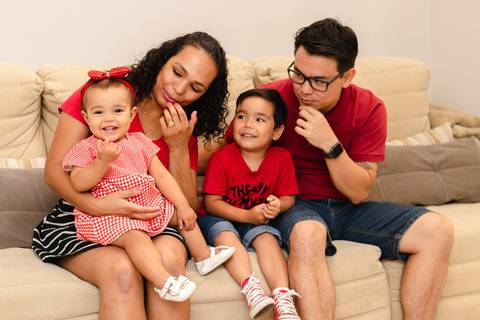 família brincando sentados no sofá de casa '