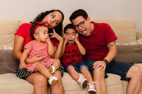 família brincando sentados no sofá de casa '