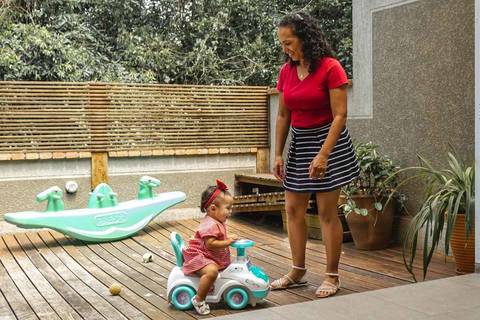 mãe brincando com o filha no velocípede no quintal de casa '