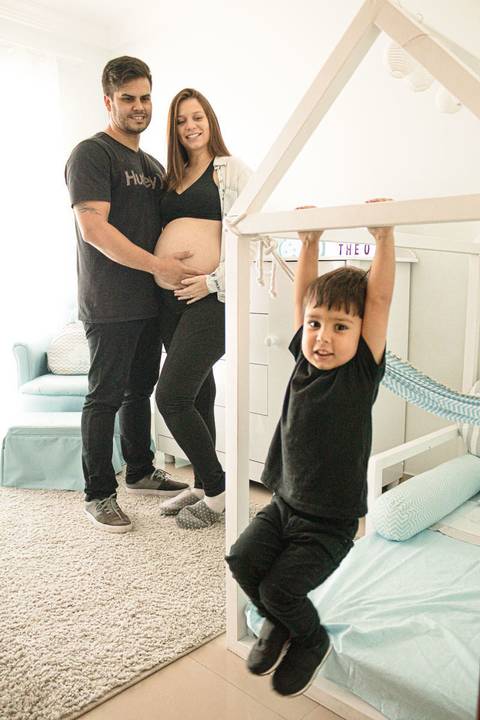 marido abraçando a mulher grávida com o filho mais novo brincando no quarto do bebê'