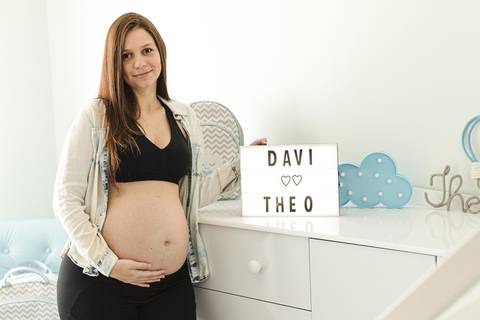 mulher grávida segurando placa com nome do bebê no quarto'