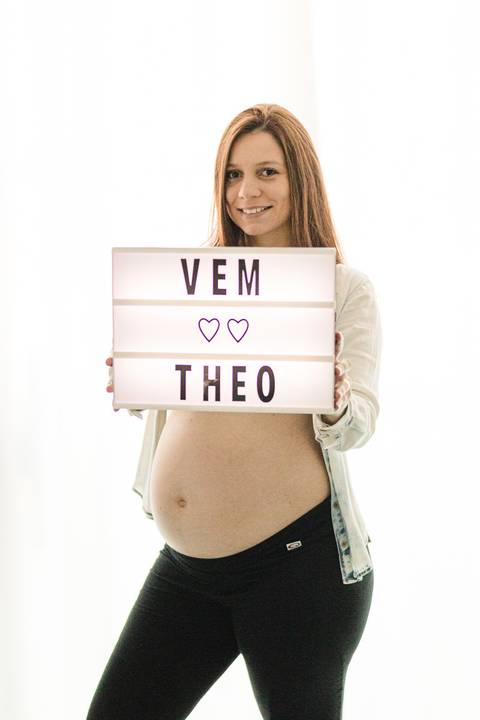 mulher grávida segurando placa com nome do bebê no quarto'
