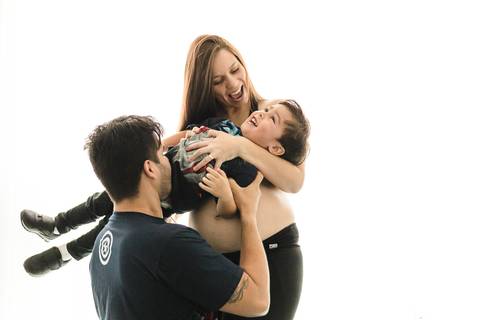 marido abraçando a mulher grávida com o filho mais novo brincando no colo'