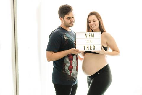mulher grávida e marido segurando placa com nome do bebê no quarto'
