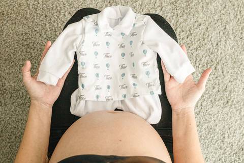 grávida segurando roupa do bebe '