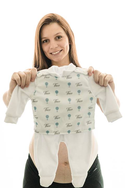 grávida segurando roupa do bebe '