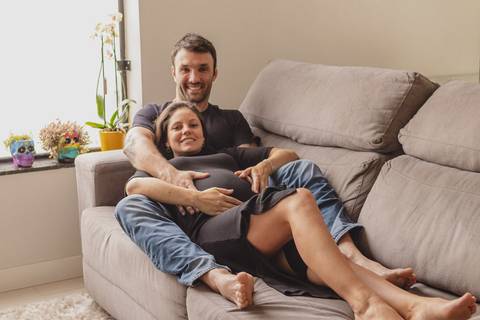 Marido e mulher grávida deitados no sofá de casa '