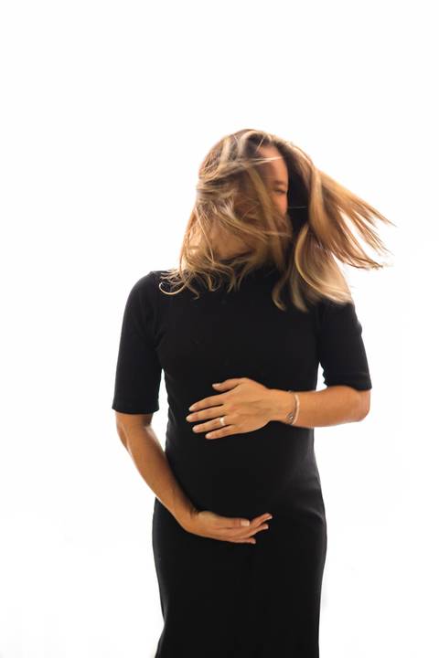 grávida abraçando a barriga e sacudindo os cabelos '