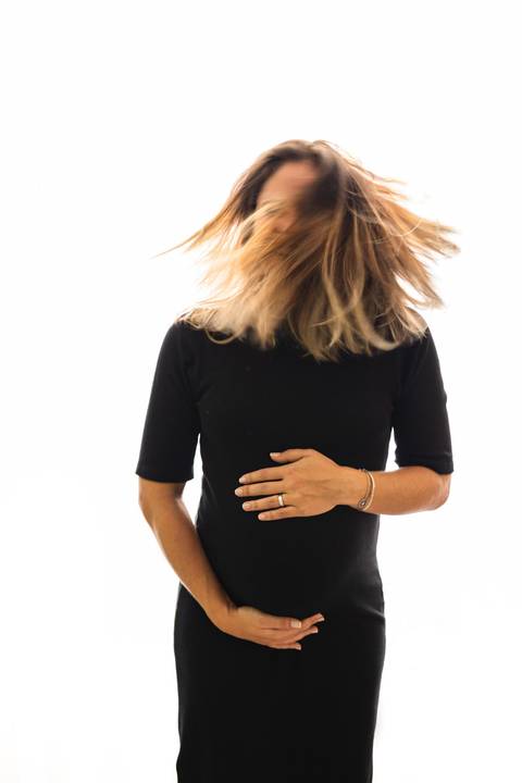grávida abraçando a barriga e sacudindo os cabelos '