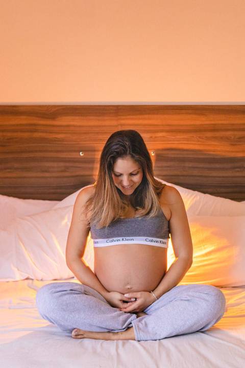 mulher grávida sentada na cama abraçando a barriga e sorrindo '