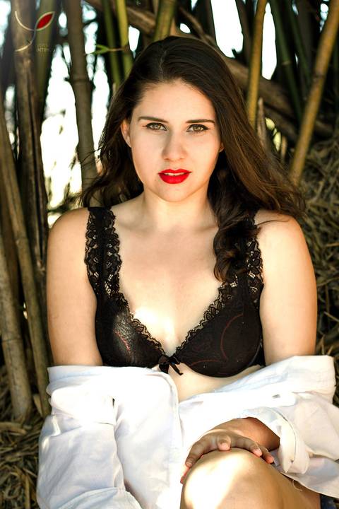 Modelo de lingerie num ensaio sensual, em meio à natureza. Com um olhar penetrante à câmera.'