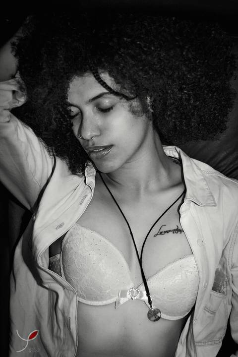 Foto sensual da modelo negra com jaqueta jeans e sutiã, cabelos crespos e longos. Numa foto em preto e branco.'
