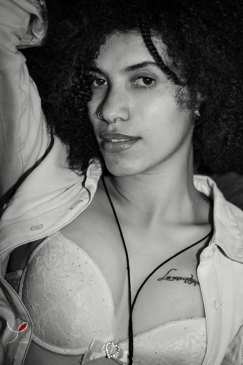 Foto sensual da modelo negra com jaqueta jeans e sutiã, cabelos crespos e longos. Numa foto em preto e branco.'