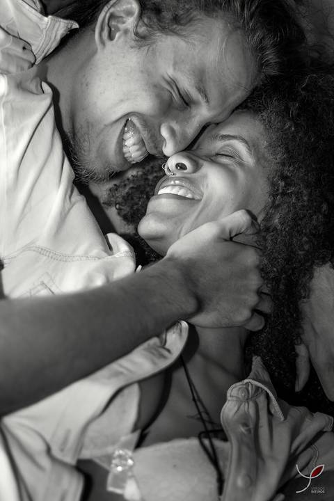 Casal olhando um para o outro. Ele sem camiseta e ela num estilo sensual. E na foto ambos estão próximos e rindo.'