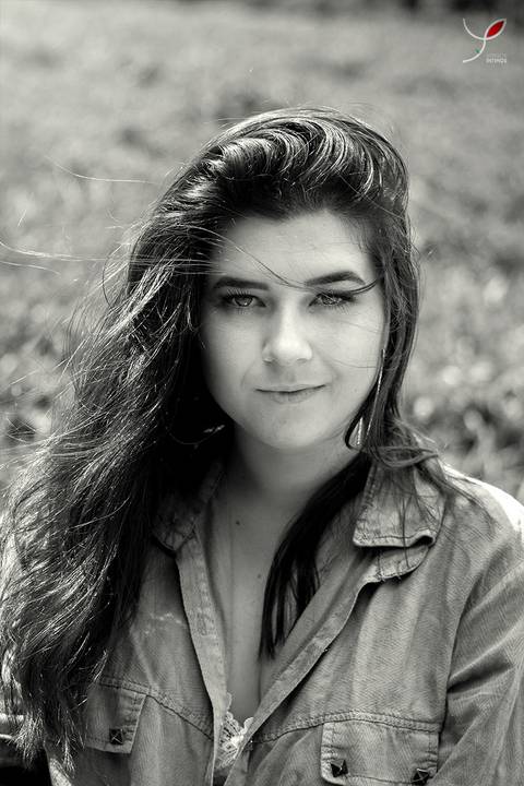 Foto em preto e branco com o rosto da modelo, marcando um olhar forte e com os cabelos voando pelo vento. E grama atrás dela.'