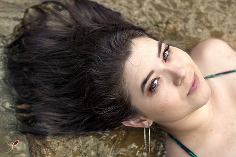 Modelo deitada nas águas de uma cachoeira de Minas Gerais. Ela está olhando para a câmera, com um olhar marcante.
'