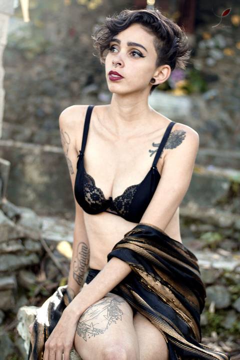 Nesta foto sensual a modelo está com um sutiã preto e um chale marrom, sentada sobre uma gruta de São José dos Campos.'