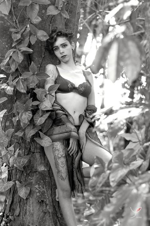 Nesta foto sensual em preto e branco a modelo está com um sutiã preto e um chale marrom, encostada numa árvore e olhando séria para o fotógrafo.'