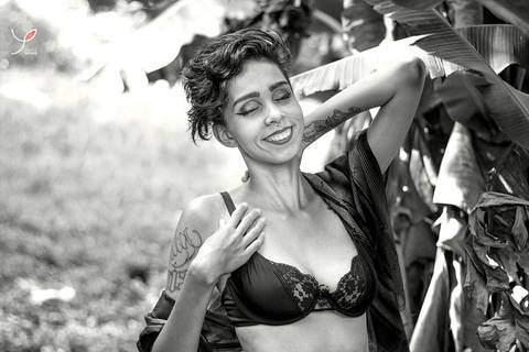 Nesta foto sensual em preto e branco a modelo está com um sutiã preto e um chale marrom, num campo e apenas sorrindo consigo mesma.'